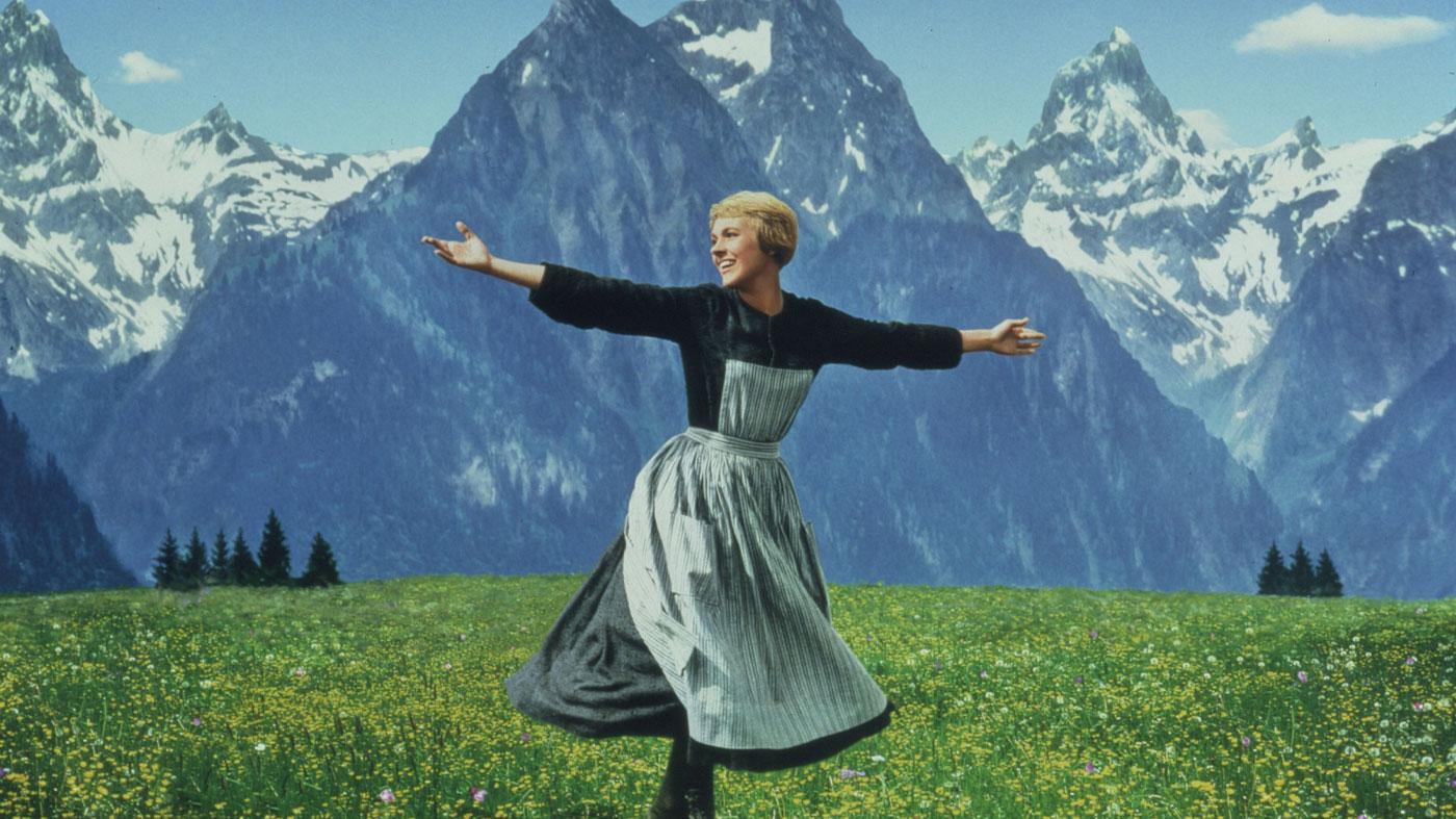 A woman in a dress dancing in a field in front of a snow capped mountain range.
